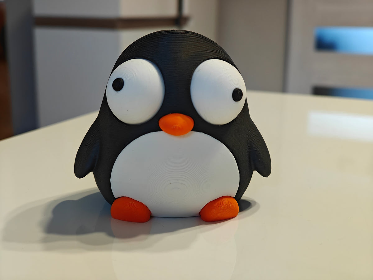 Liten pingvinfigur med rörliga ögon på ett skrivbord bredvid en kaffemugg