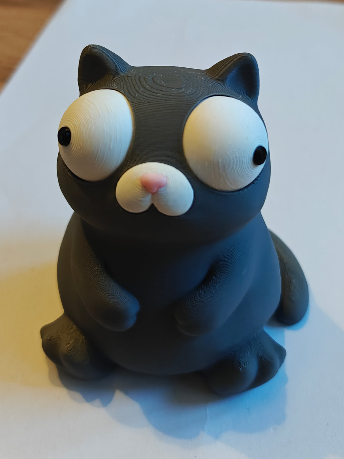Närbild av en knubbig vit kattfigur med stora rörliga googlyögon