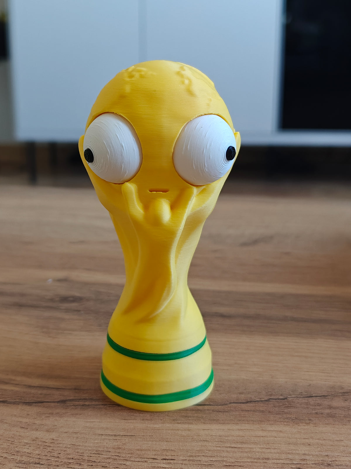Närbild av en rolig VM-pokalfigur med ett stort rörligt googlyöga, framifrån