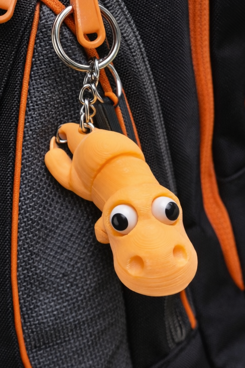 Orange 3D-printad dinosaurienyckelring med googlyögon och metallring