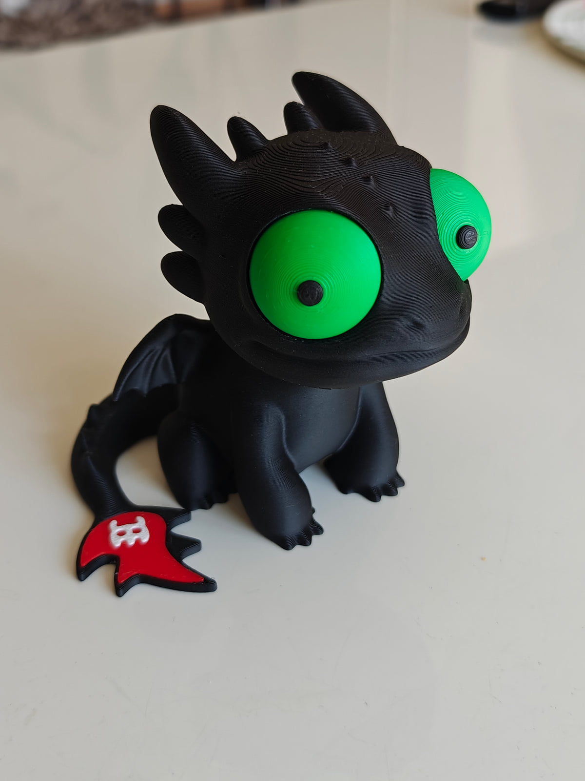 Tandlöse-drakfigur med stora rörliga ögon, framifrån mot vit bakgrund