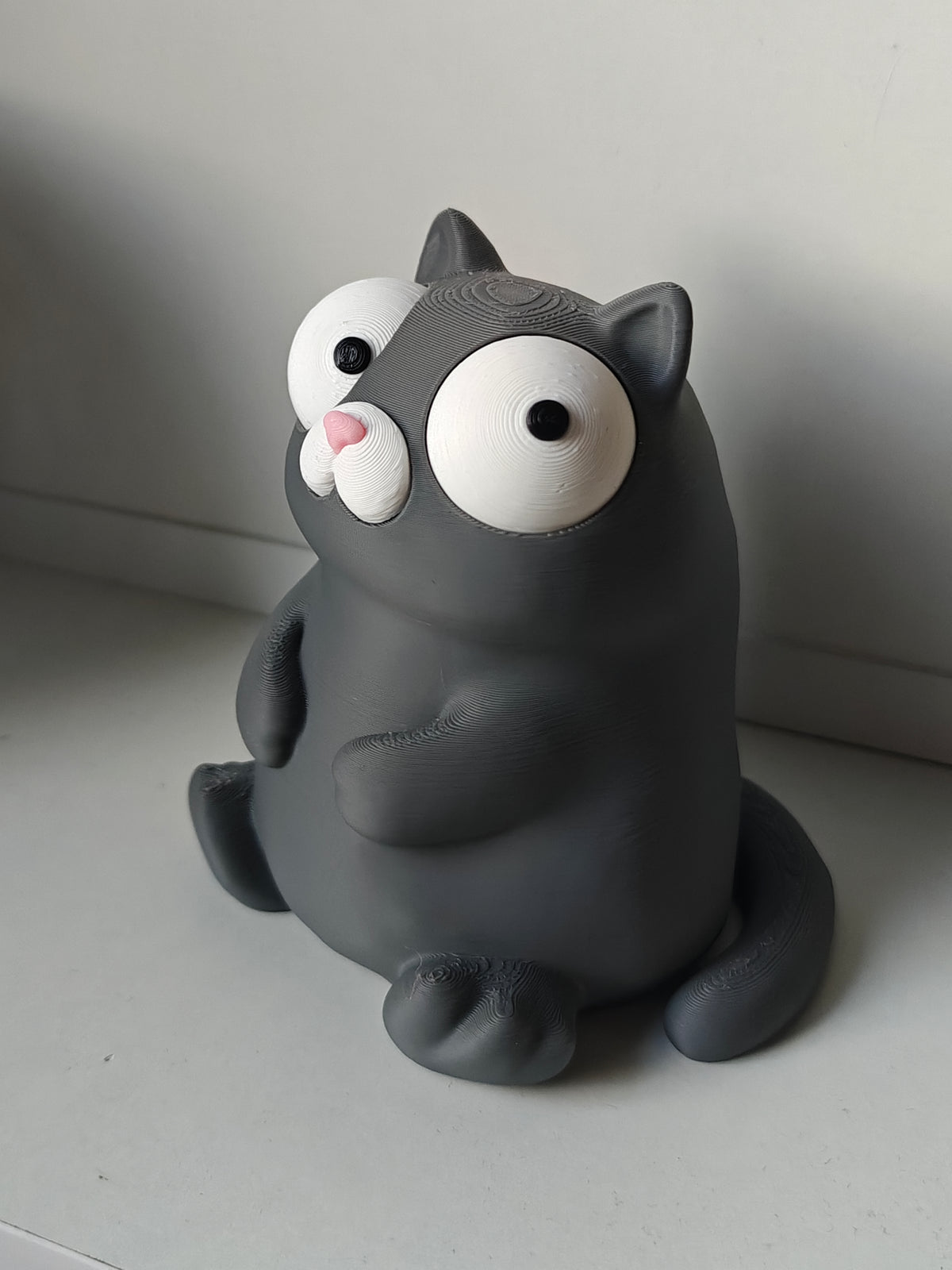 Tokig kattfigur med rörliga ögon på skrivbord bredvid kaffemugg