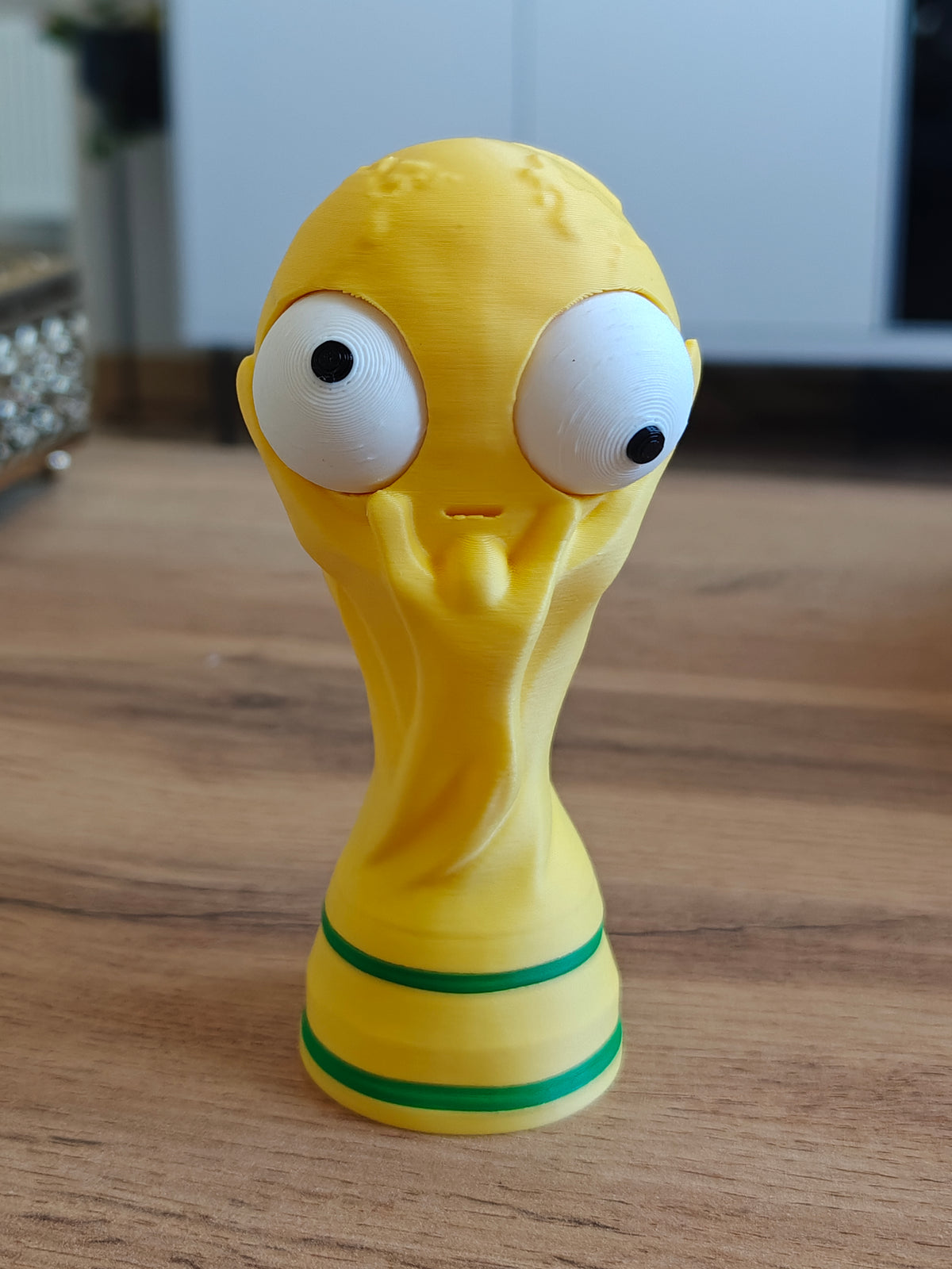 Närbild av en rolig VM-pokalfigur med ett stort rörligt googlyöga, framifrån