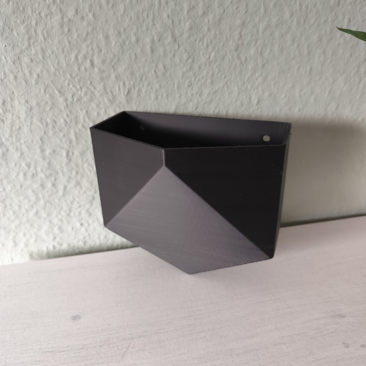 Low poly-väggkruka monterad på en vit vägg med en liten krukväxt