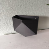 Low poly-väggkruka monterad på en vit vägg med en liten krukväxt