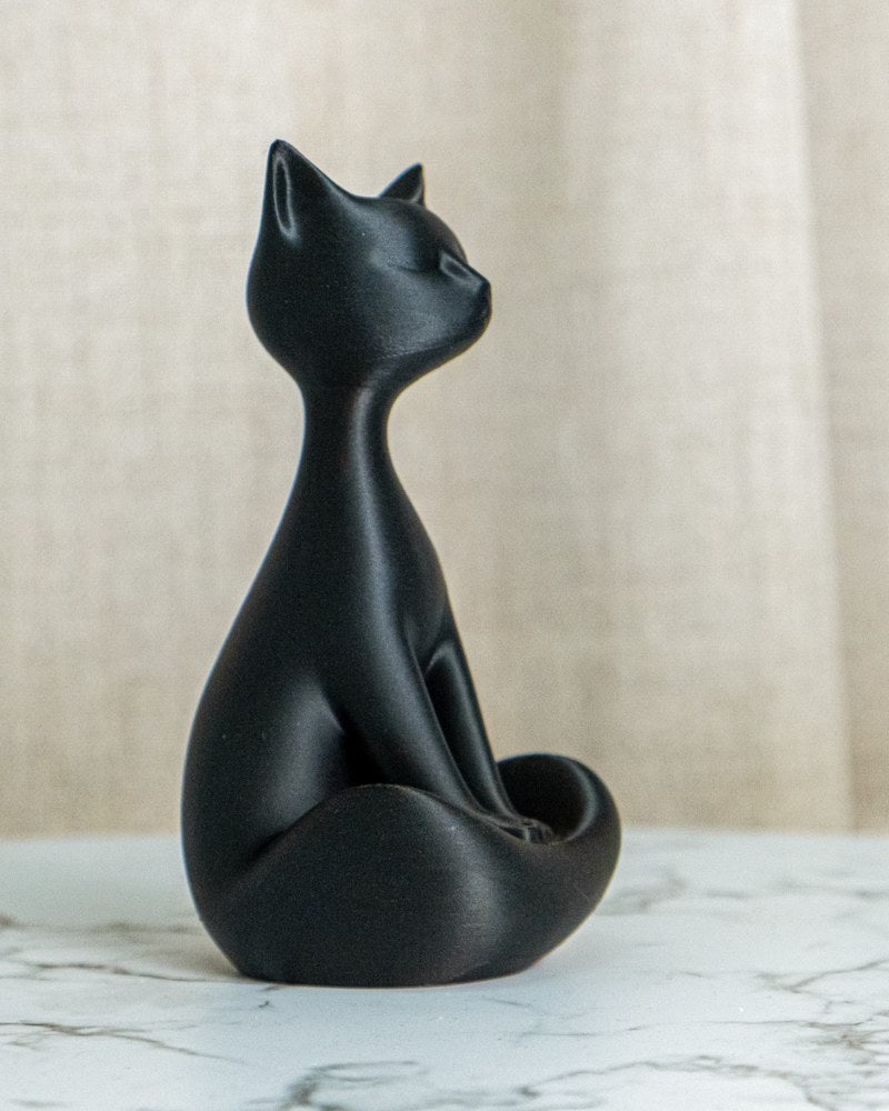Närbild av en matt svart kattskulptur som sitter upprätt mot vit bakgrund