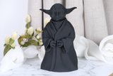 Yoda-skulptur på ett skrivbord i trä bredvid en liten växt och en bokhög