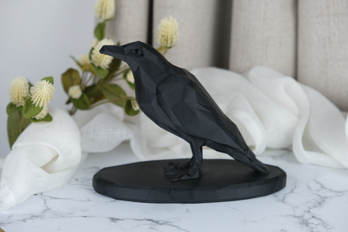 Low poly-kråkskulptur på en trähylla med ljus och mörk keramik
