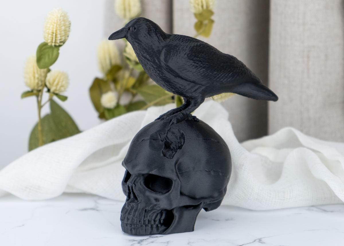 Skulptur av en korpskalle på en mörk trähylla med ljus och torkade växter