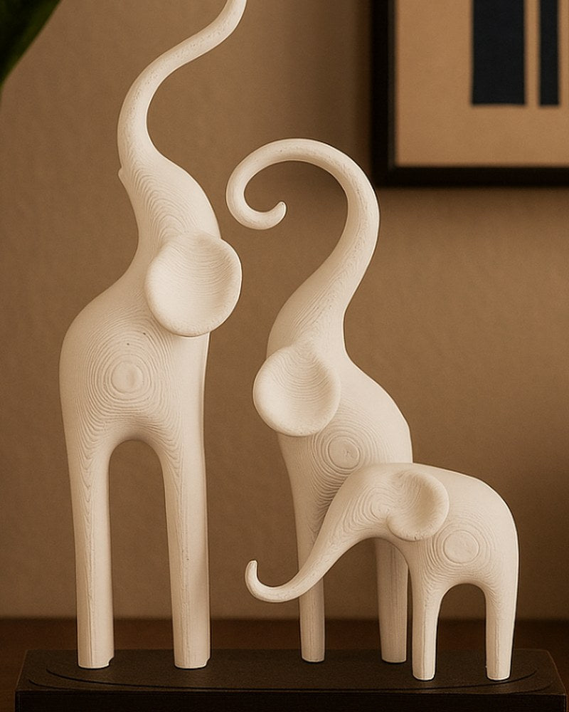 Minimalistisk elefantskulptur med tre stiliserade figurer på mörk sockel, vit bakgrund, närbild
