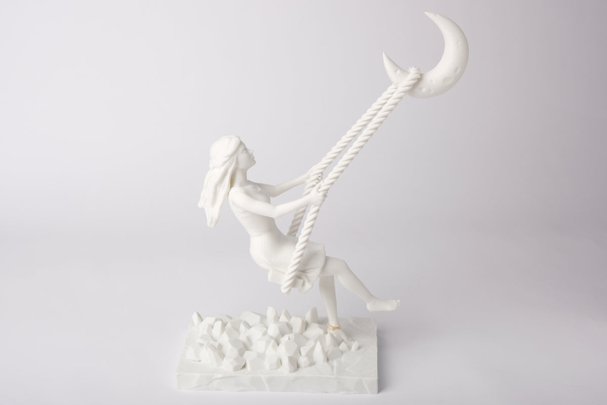Skulptur med halvmånegunga på ett nattduksbord bredvid ett ljus och torkade blommor
