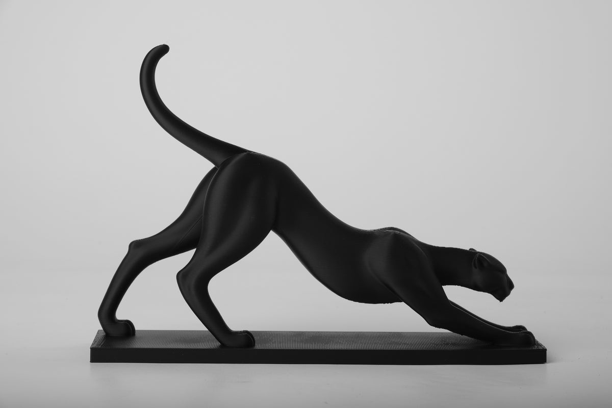Skulptur av en panter som sträcker på sig, på en trähylla med böcker och keramik