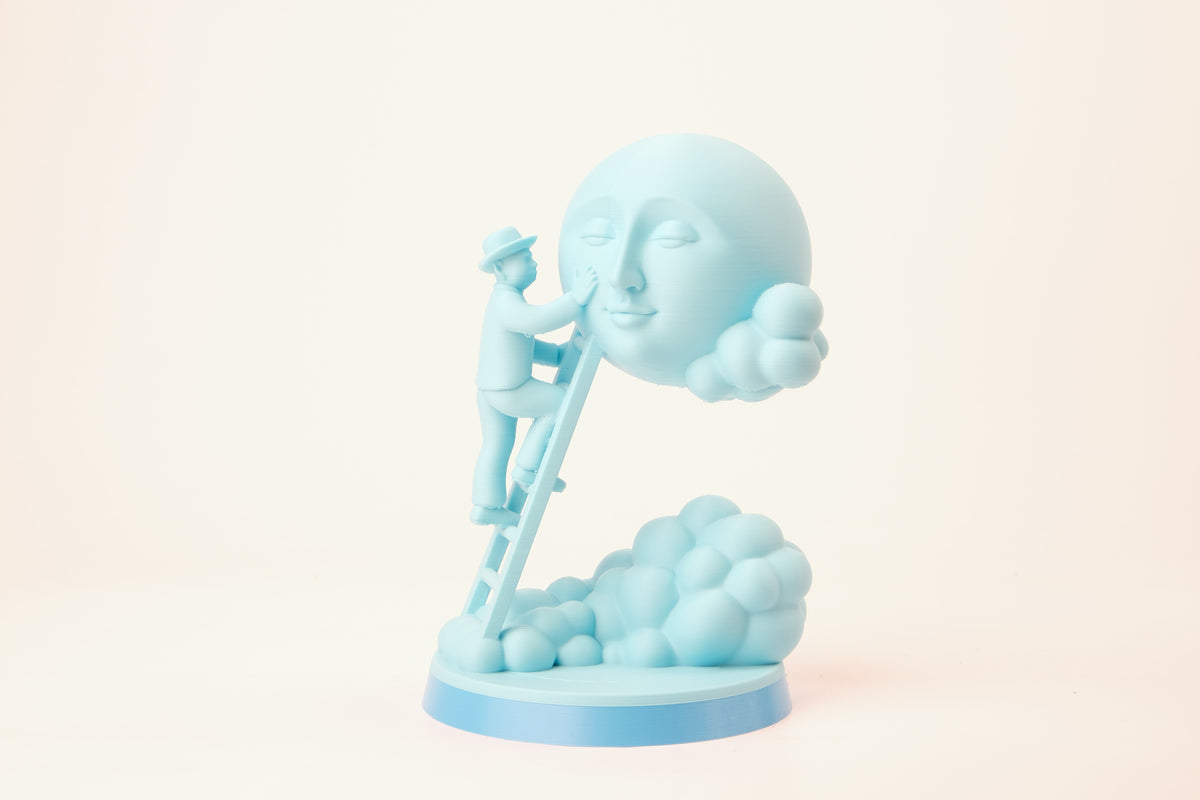 Moon Caretaker-skulptur på en minimalistisk hylla mellan böcker och en liten växt