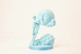 Moon Caretaker-skulptur på en minimalistisk hylla mellan böcker och en liten växt
