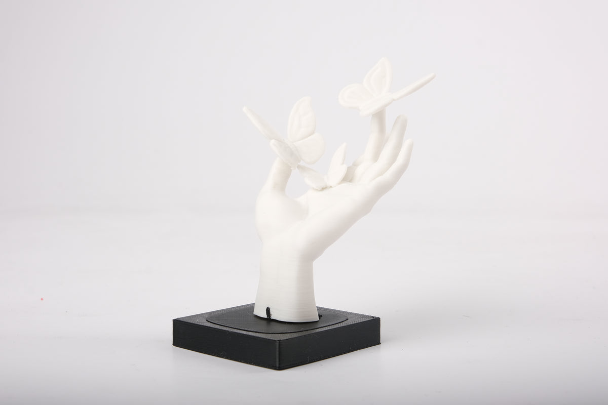 Handskulptur med fjärilar på en minimalistisk trähylla bredvid en liten keramikvas