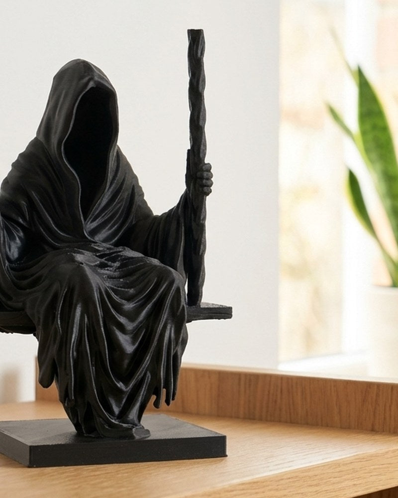 Skulptur av liemannen i matt svart, sittande på gunga, framifrån