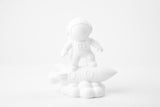 Skulptur av astronaut på raket på ett minimalistiskt skrivbord bredvid en växt och små böcker