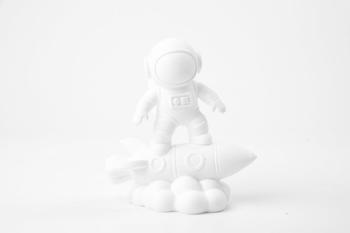 Skulptur av astronaut på raket på ett minimalistiskt skrivbord bredvid en växt och små böcker