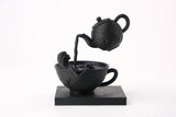 Skulpturen Tea Time Reverie på en mörk hylla med böcker och minimalistisk inredning