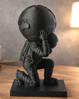 Mattsvart Atlas-skulptur av en knästående astronaut som håller ett klot, mot neutral bakgrund