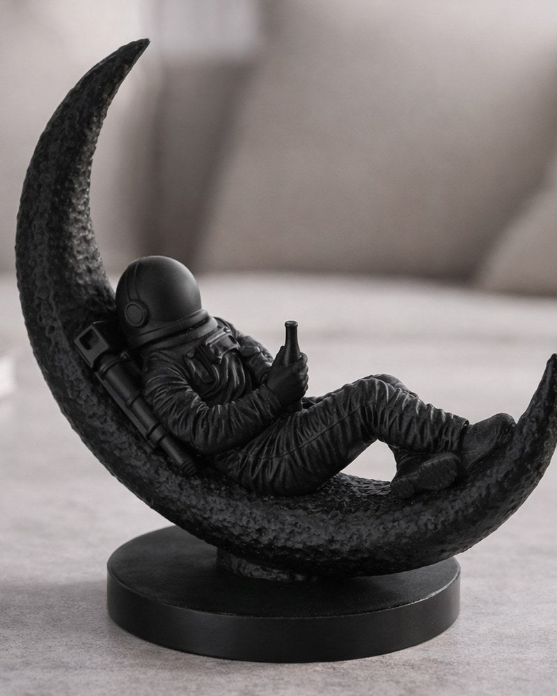 Astronautskulptur som sitter på en halvmåne, matt yta, närbild mot vit bakgrund