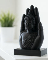 Mattsvart buddhahandskulptur på vit yta med en stilla figur som vilar i den öppna handflatan