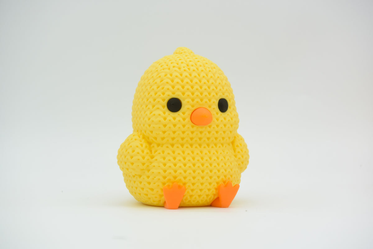 Närbild av en liten gul stickad kyckling med orange näbb och fötter