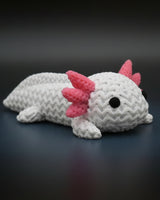 Liten stickad axolotl på en trähylla bredvid böcker och en växt i skandinavisk inredning