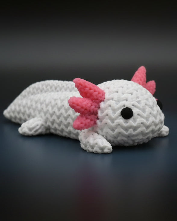Liten stickad axolotl på en trähylla bredvid böcker och en växt i skandinavisk inredning