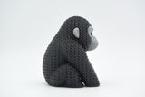 Stickad gorillafigur på en trähylla bredvid böcker och en liten växt