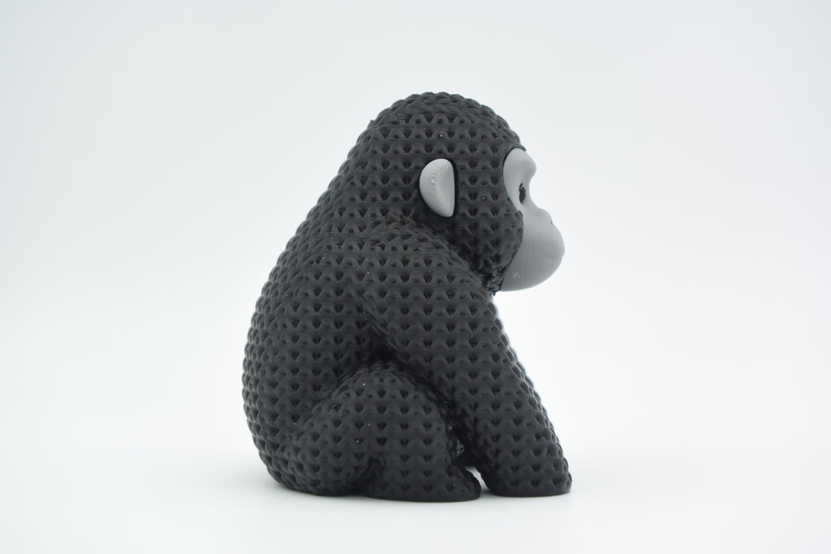 Stickad gorillafigur på en trähylla bredvid böcker och en liten växt