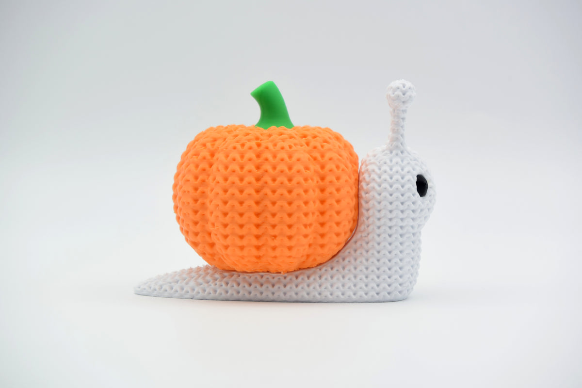 Stickad pumpasnigel som halloweendekoration på en trähylla med torkade höstlöv och små ljus