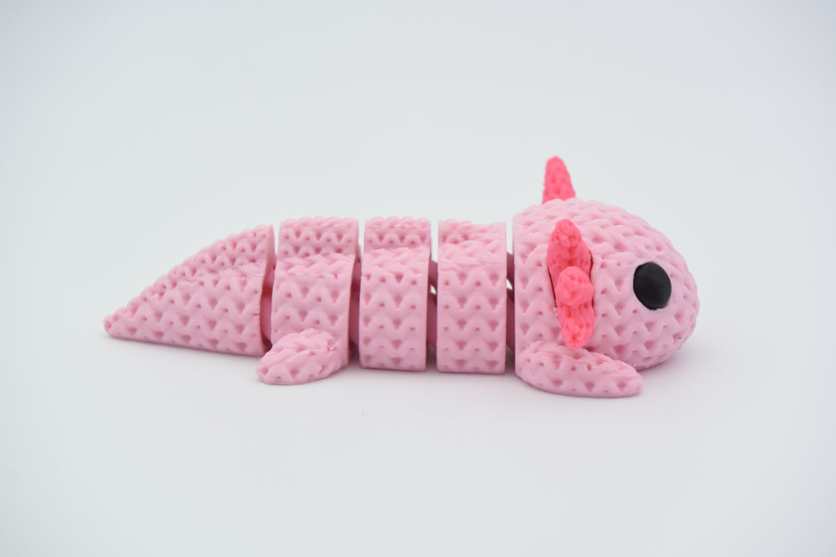 Stickad flexi-axolotl på trähylla bredvid liten växt