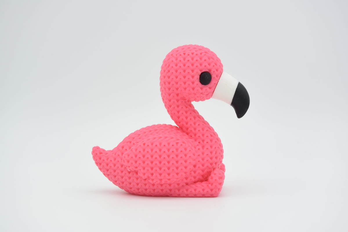 Stickad flamingofigur på en trähylla bredvid en liten växt och neutral inredning