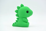 Grön stickad stegosaurusfigur på trähylla bredvid små växter och böcker