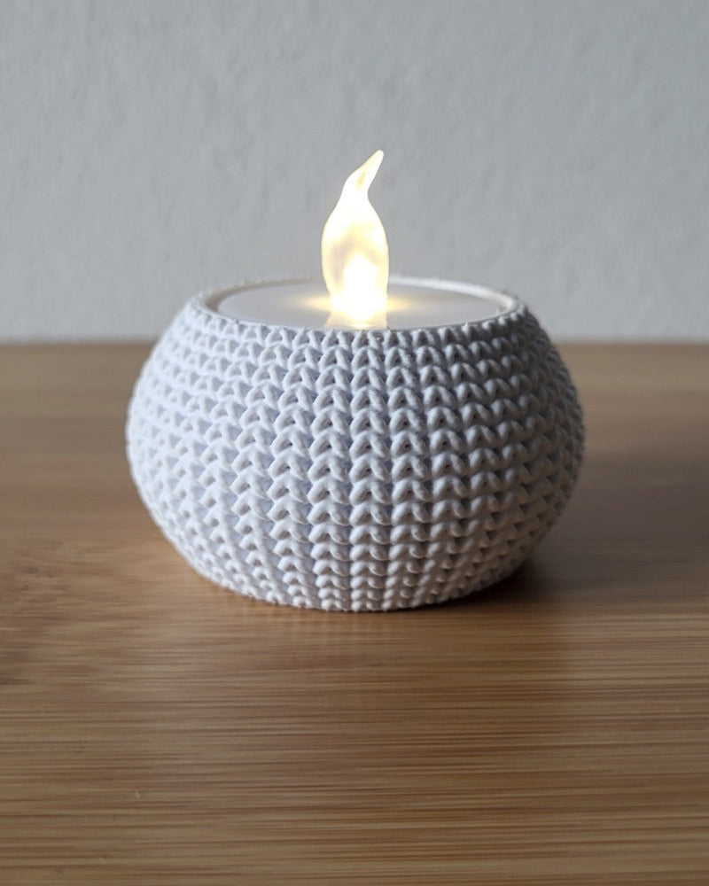 Närbild av en stickad ljushållare med mjuk vävd textur, otänd, på vit yta