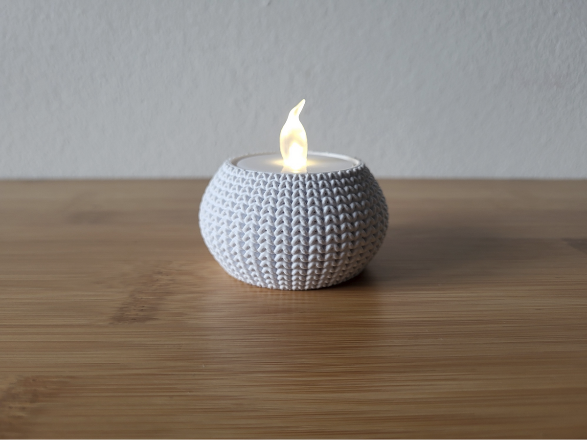 Närbild av en stickad ljushållare med mjuk vävd textur, otänd, på vit yta