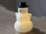 Snögubbe med hatt och näsa över ett LED-värmeljus