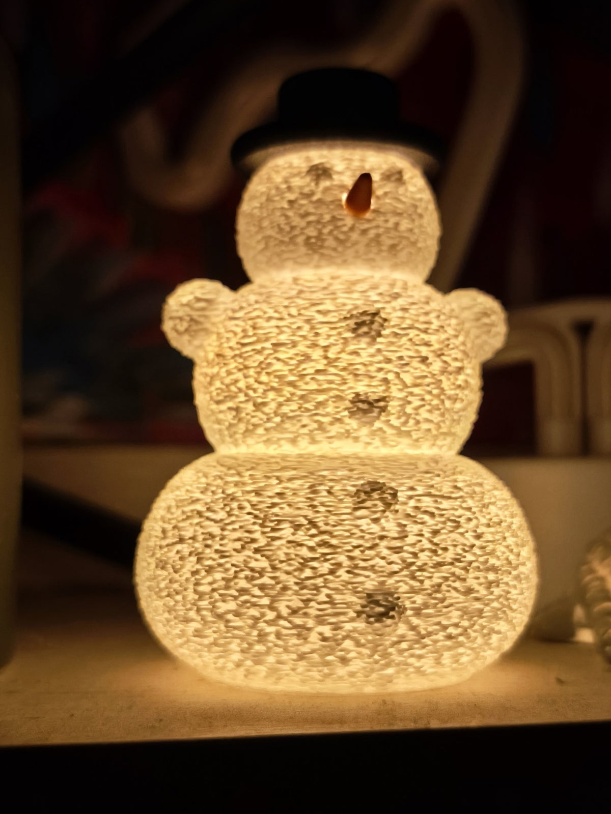 Snögubbe med hatt och näsa över ett LED-värmeljus